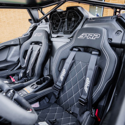 2026 Can-Am Maverick R, Green / Black, close-up of the cabin featuring two black PRP bucket seats with white stitching and racing harnesses.