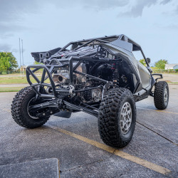 2026 Can-Am Maverick R, green and black side-by-side off-road vehicle shown from the rear with exposed suspension, roll cage, and rugged tires