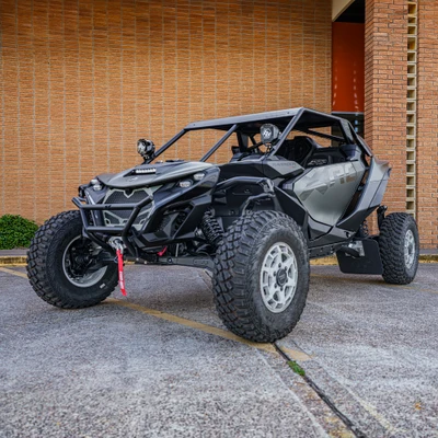 2026 Can-Am Maverick R, green and black side-by-side off-road vehicle with rugged tires and roll cage parked outside a brick building