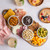 Four mini white bowls on a charcuterie board filled with snacks and cheese