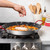 paella pan with hand sprinkling saffron rice, shrimp, mussels, and vegetables arranged on stovetop