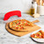 lifestyle scene of freshly cut supreme topping pizza on cutting board placed on marble countertop with rock the boat pizza cutter in background