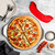 overhead lifestyle scene of sliced supreme topping pizza on pizza pan staged on marble countertop next to rock the boat pizza cutter and various seasonings
