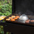 cheese melting dome placed on outdoor grill with burger patties and buns
