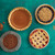 Four baked pies in Nordic Ware aluminum pie pans with pie shield, showing different fillings and crust styles