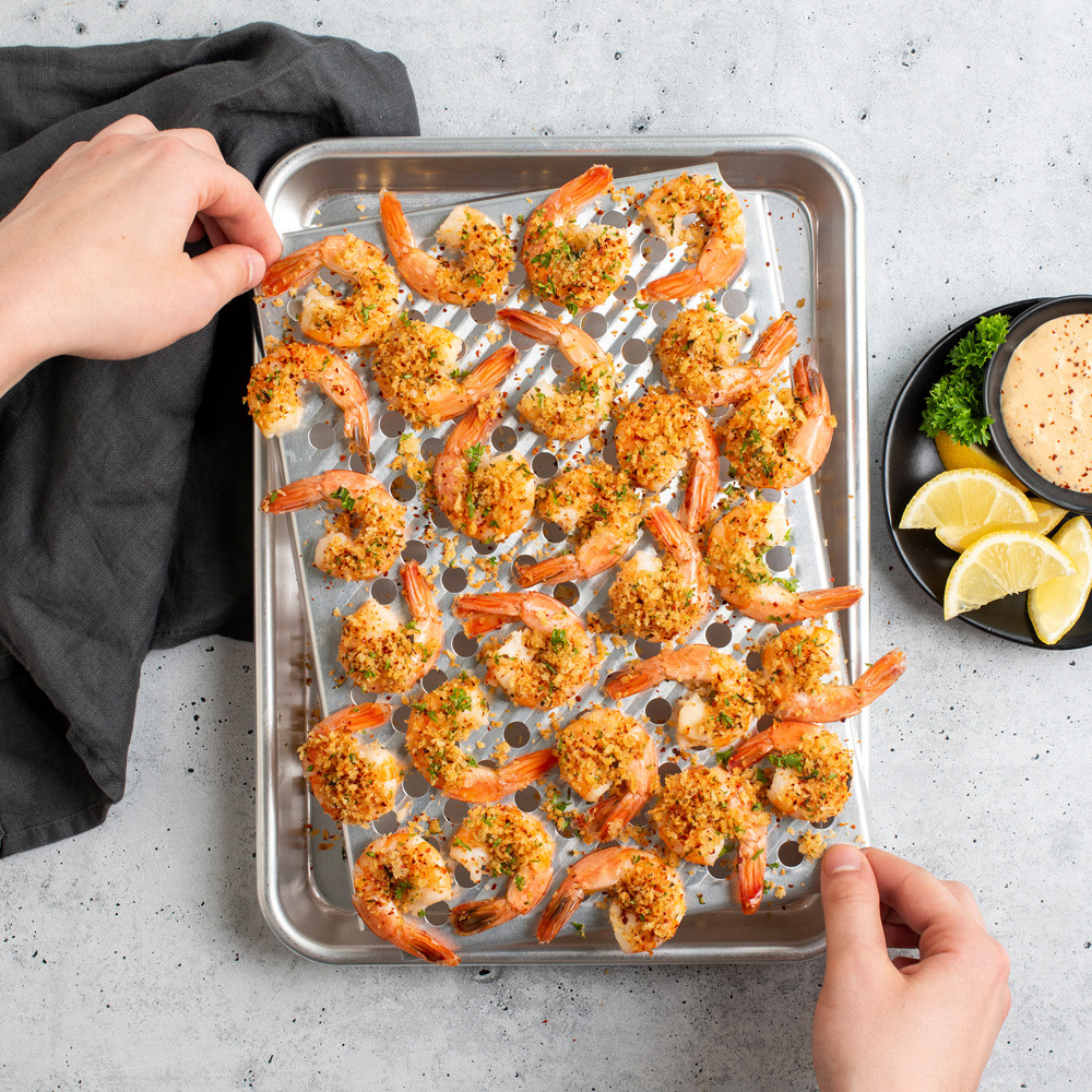 Overhead image of Quarter Sheet & Multi Task Rack with shrimp, hands holding rack over pan, sliced lemons and sauce next to pan