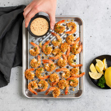 Overhead image of  Quarter Sheet & Multi Task Rack with shrimp, hand placing sauce on rack, sliced lemons next to pan