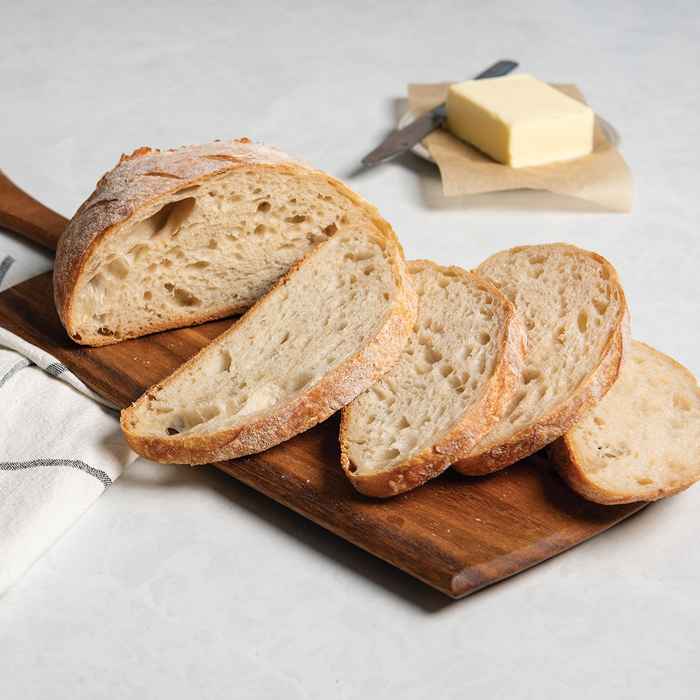 Sliced sourdough bread on cutting board, stick of butter in background