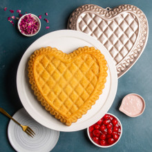Overhead of plain quilted heart cake on white cake stand with Pan, petals, dish of cherries, and pink icing around