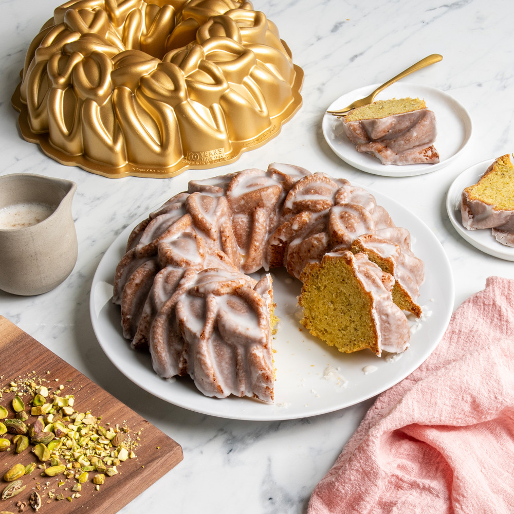 Glazed Laurel Wreath Bundt on white plate, cut, pistachios on cutting board, pieces of cake on small white plates
