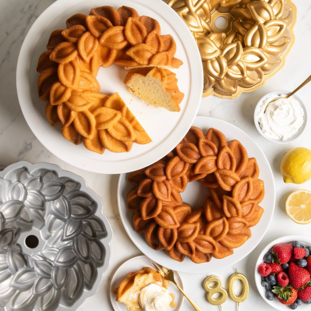 Overhead image of two baked Laurel Wreath bundt cakes on cake platters with Bundt pan and ingredients in background