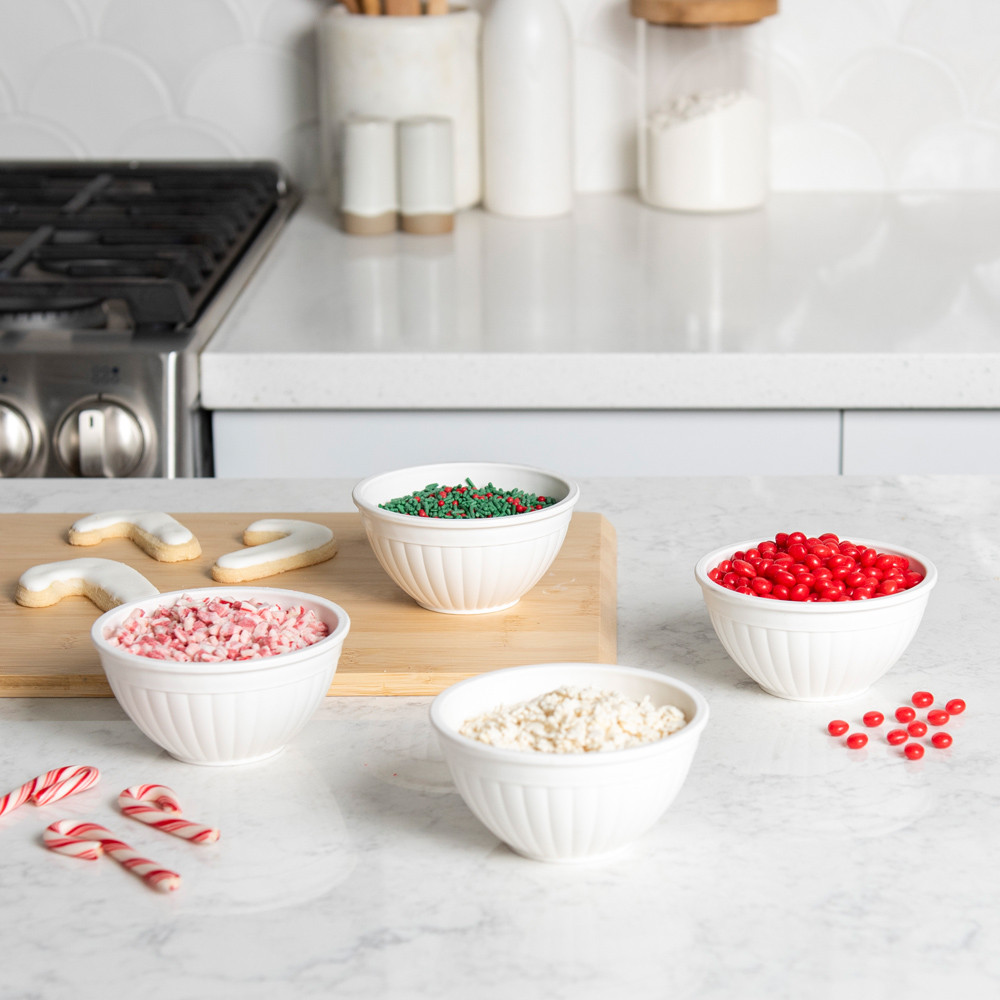 Four white mini bowls arranged on white countertop with crushed candy cane, red and green sprinkles, and red candies 