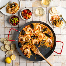 paella pan with saffron rice, shrimp, mussels, and vegetables displayed on tile countertop, wooden spoon in pan with two plated portions