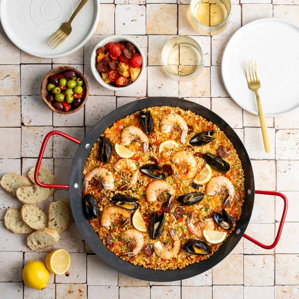paella pan with saffron rice, shrimp, mussels, and vegetables displayed on tile countertop