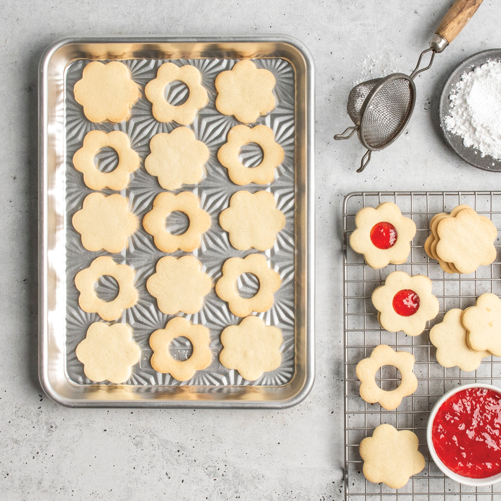 overhead of novelty shape cookies on starburst quarter sheet pan; cooling grid with jam nearby