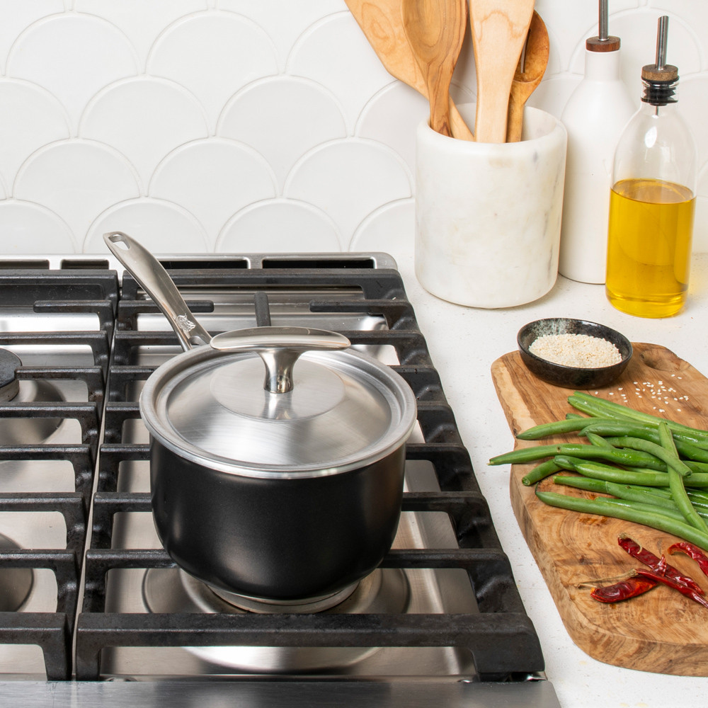 basalt 1.5qt saucepan with lid on stovetop, cutting board with ingredients next to stove on countertop