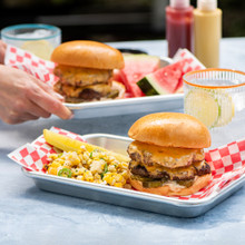 double cheese burgers with veggies being served by hand on nordic ware burger trays