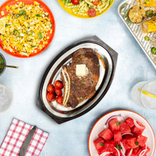 overhead of cooked steak placed on sizzling steak server plate surrounded by various bbq dishes