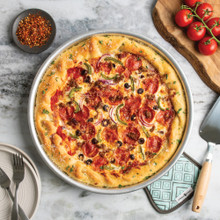 nordic ware deep dish pizza pan with supreme style pizza next to cake server and hot pad