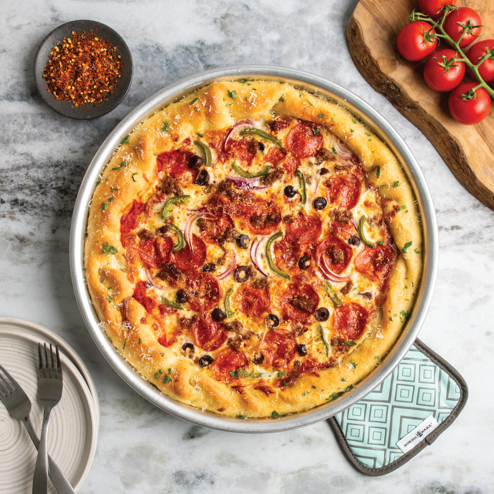nordic ware 14 inch deep dish pizza pan with pizza placed on cotton hot pad with silicone geometric detailing
