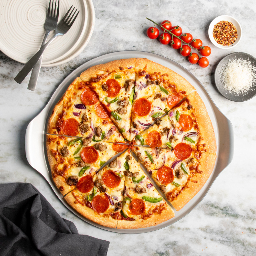 nordic ware aluminized steel pizza & baking steel pan displayed on countertop with freshly baked and cut pizza with toppings