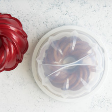Red Nordic Ware aluminum bundt pan with white translucent plastic cake keeper dome, cake inside keeper