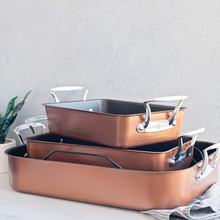 Three Nordic Ware copper roasters in graduated sizes stacked together with kitchen towel, showing rounded rectangular shape