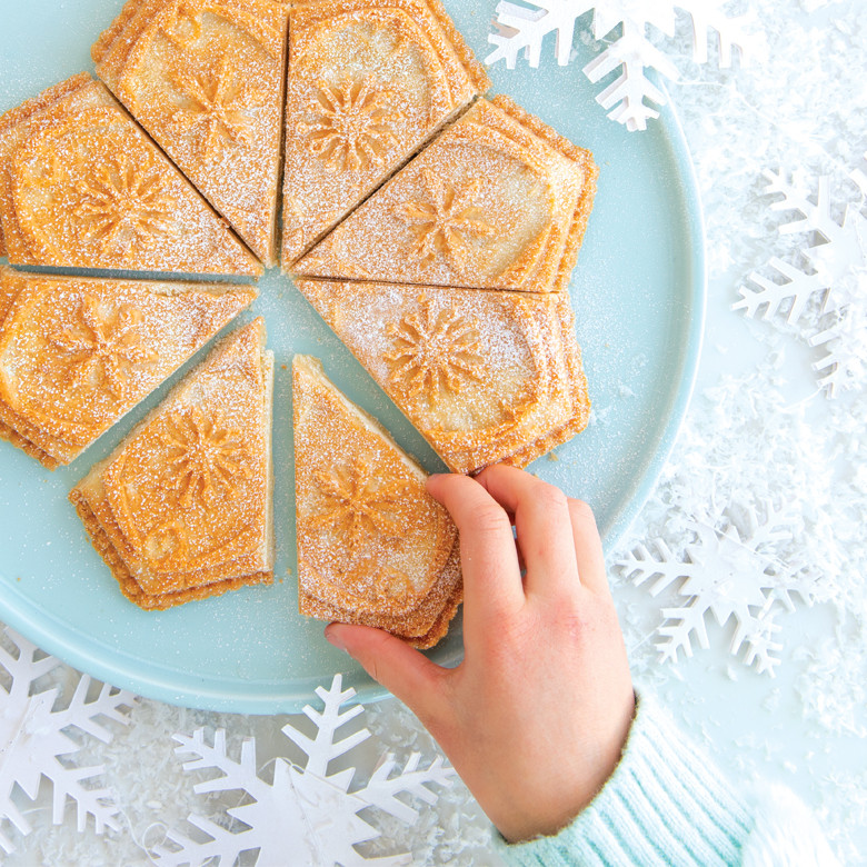 Eight golden diamond-shaped shortbread cookies baked in Nordic Ware snowflake pan, hand reaching for one piece