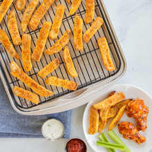 Golden baked potato fries on Nordic Ware aluminum baking tray with chicken wings and celery served alongside