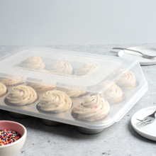 Angled image of vanilla cupcakes in muffin pan with high dome lid on top.