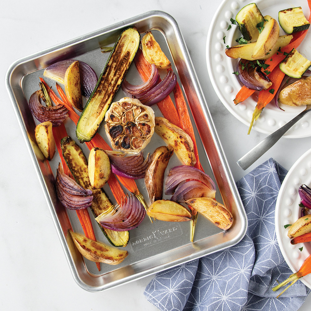 Nordic Ware aluminum quarter sheet pan with golden roasted vegetables including carrots, potatoes, and Brussels sprouts