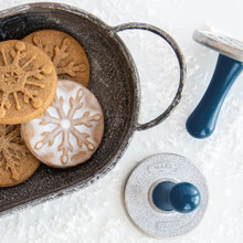Round sugar cookies with detailed snowflake patterns stamped on surface, displayed on white plate with cookie stamps nearby