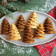 Six golden tree-shaped cakelets from Nordic Ware Evergreen pan arranged on white platter with winter styling
