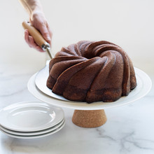 Golden swirl bundt cake on white pedestal stand with Nordic Ware stainless steel cake lifter tool underneath