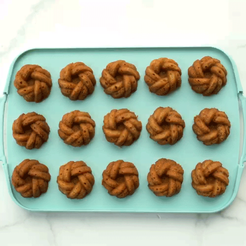 Nordic Ware powdered sugar duster sprinkling white sugar over golden mini bundt cakes on cooling rack