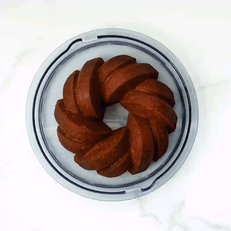 Clear plastic dome cake keeper with white base containing golden bundt cake with fluted ridges