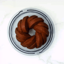Clear plastic dome cake keeper with white base containing golden bundt cake with fluted ridges