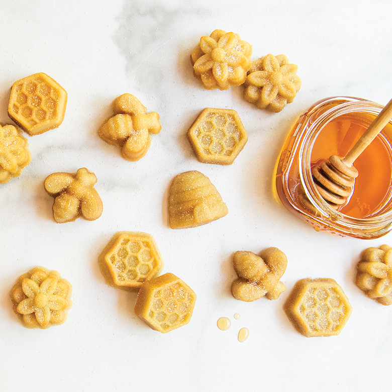 Golden bee-shaped bitelets baked in Nordic Ware aluminum pan, arranged on marble surface with honey jar