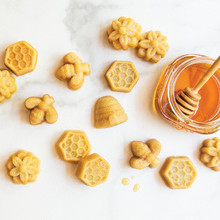 Golden bee-shaped bitelets baked in Nordic Ware aluminum pan, arranged on marble surface with honey jar