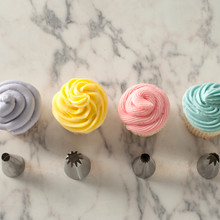 Four cupcakes with white frosting piped using different decorating tips showing rosette, star, leaf, and round designs