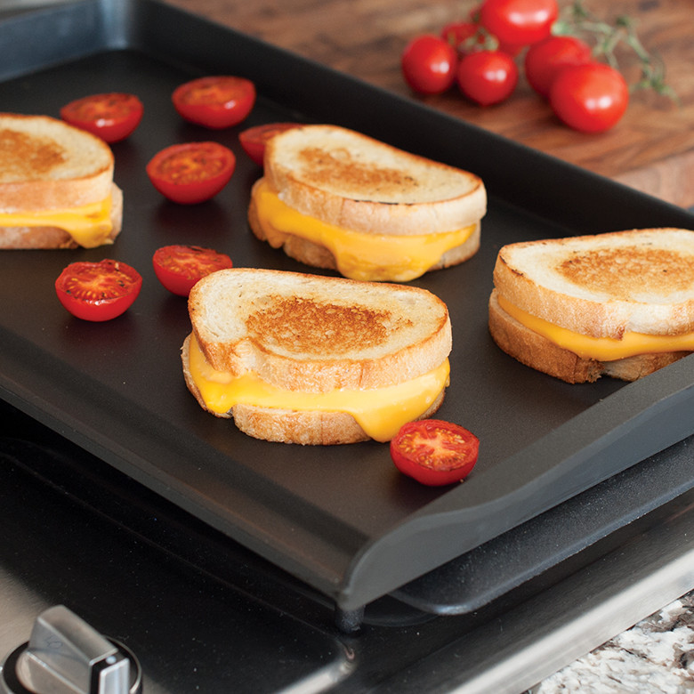 Nordic Ware aluminum double backsplash griddle on stovetop with golden grilled cheese sandwiches and caramelized tomato slices