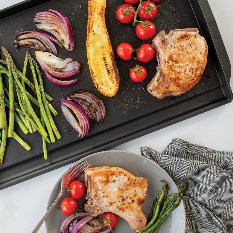 Nordic Ware double backsplash griddle with seared pork chops and colorful vegetables, plated serving alongside