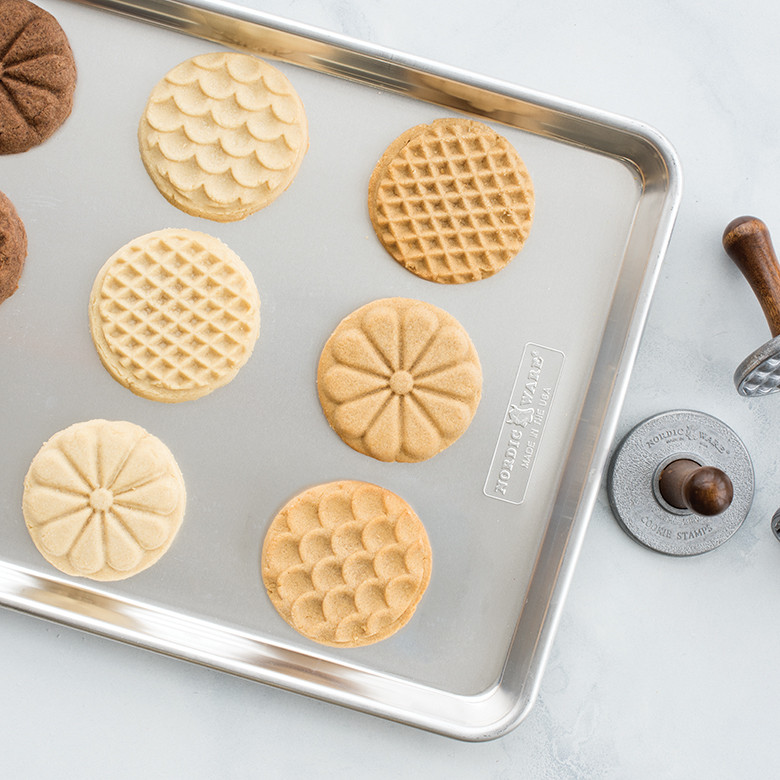 Golden baked cookies with decorative stamped patterns arranged on aluminum baking sheet
