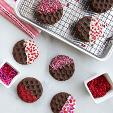 Round cookies with decorative stamped patterns, half dipped in white chocolate and colorful sprinkles on baking sheet