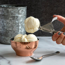 Hand using Nordic Ware large cookie scoop with spring-loaded handle to serve vanilla ice cream into white bowl