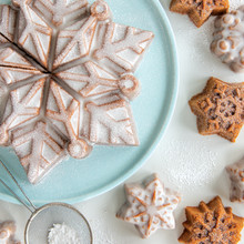Glazed snowflake-shaped cake and mini cakelets dusted with powdered sugar on blue platter