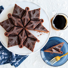 Chocolate bundt cake with intricate snowflake design from Nordic Ware pan, slice cut and plated beside coffee cup