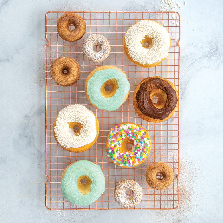 Assorted glazed and plain donuts cooling on wire rack, baked in Nordic Ware classic donut pan
