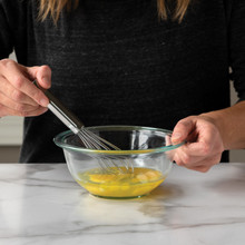 Nordic Ware small stainless steel whisk beating raw yellow eggs in white ceramic bowl