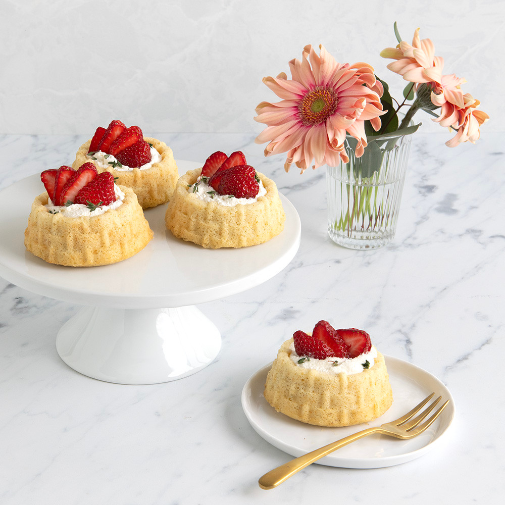 Three golden shortcake basket cakes baked in Nordic Ware pan, topped with whipped cream and fresh strawberry slices